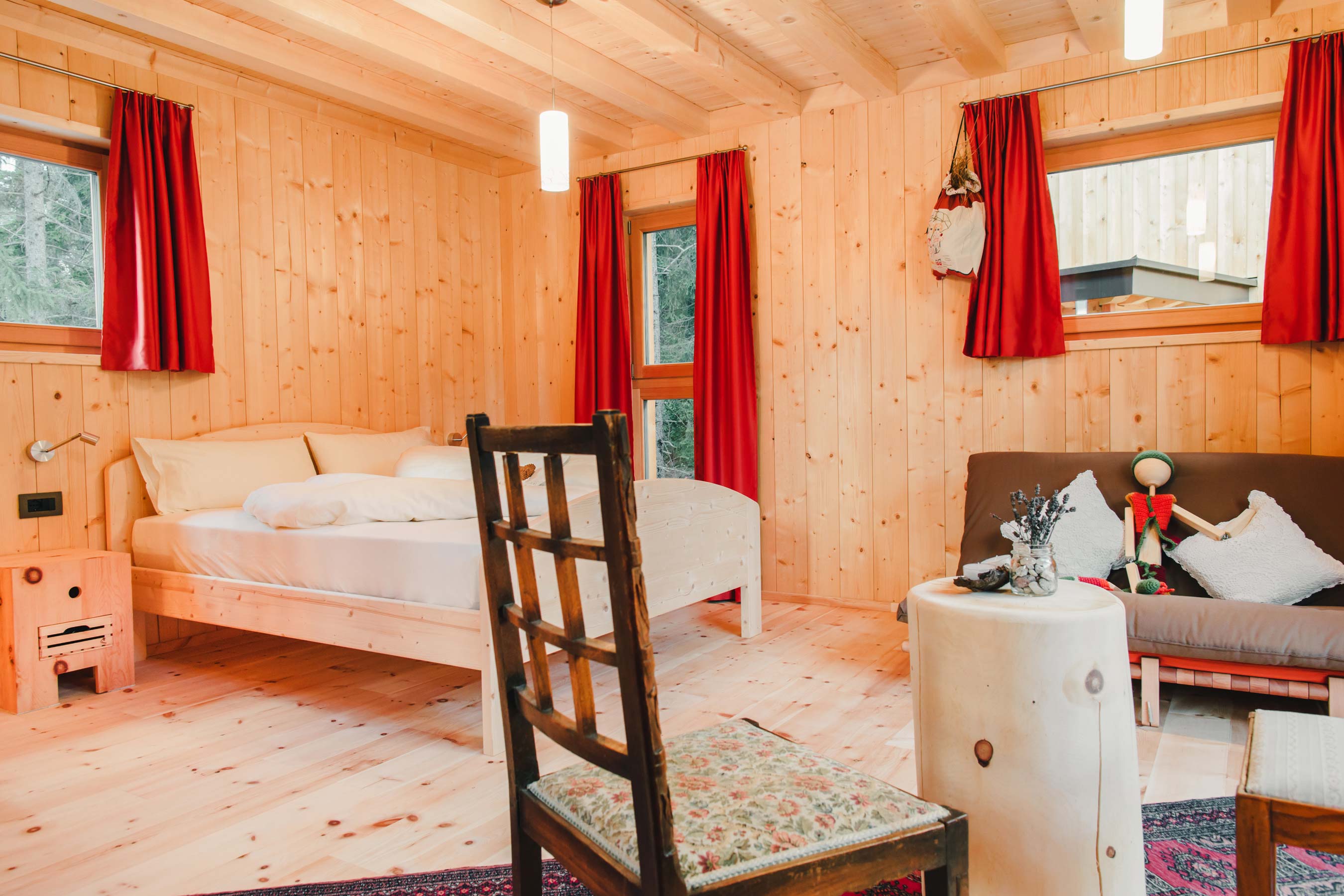 Cozy wooden room with a bed, chair, sofa, and red curtains.